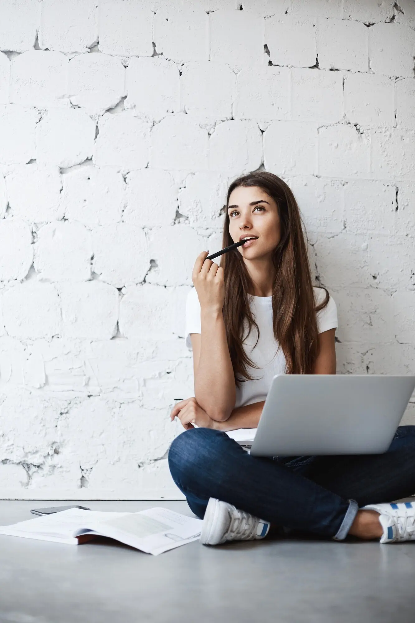 Porträt einer jungen, verträumten Studentin, die an einem Stift kaut und sich am Laptop auf ihre Abschlussprüfungen vorbereitet. Bildungskonzept.